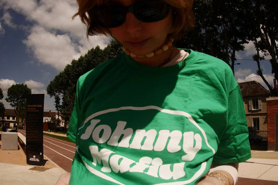 Person wearing a green 'Johnny Mafia' t-shirt outdoors on a sunny day.